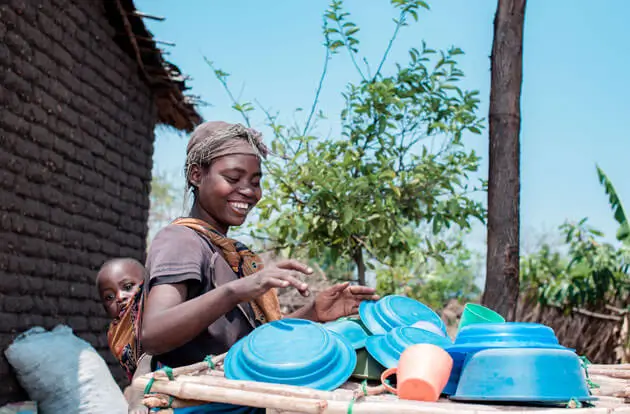 DEICHMANN-Stiftung | Malawi – Opportunity International Deutschland zeigt Menschen in extremer Armut den Weg in ein besseres Leben Malawi – Frau mit auf dem Rücken gebundenen Kind kümmert sich im Freien um Abwasch