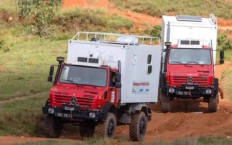 DEICHMANN-Stiftung | Madagascar Mobile Clinic – Gesundheitsangebote erreichbar machen – geländegängige Fahrzeuge – Unimog Alt-Tag Madagascar Mobile Clinic – zwei geländegängige Fahrzeuge vom Typ Unimog fahren über eine schlammige, buckelige Lehmpiste