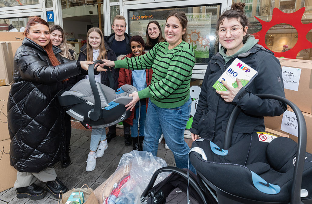 deichmann-stiftung-projekt-Gesundheit-fruehe-hilfen-duisburg junge Frau überreicht anderer Frau Sitzschale für Baby