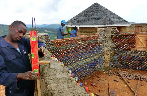 DEICHMANN Stiftung | Sozialunternehmen Uganda – Kreislaufwirtschaft Sozialunternehmen Uganda – Eine Person im Bildvordergrund baut eine Mauer aus Plastikflaschen - Kreislaufwirtschaft